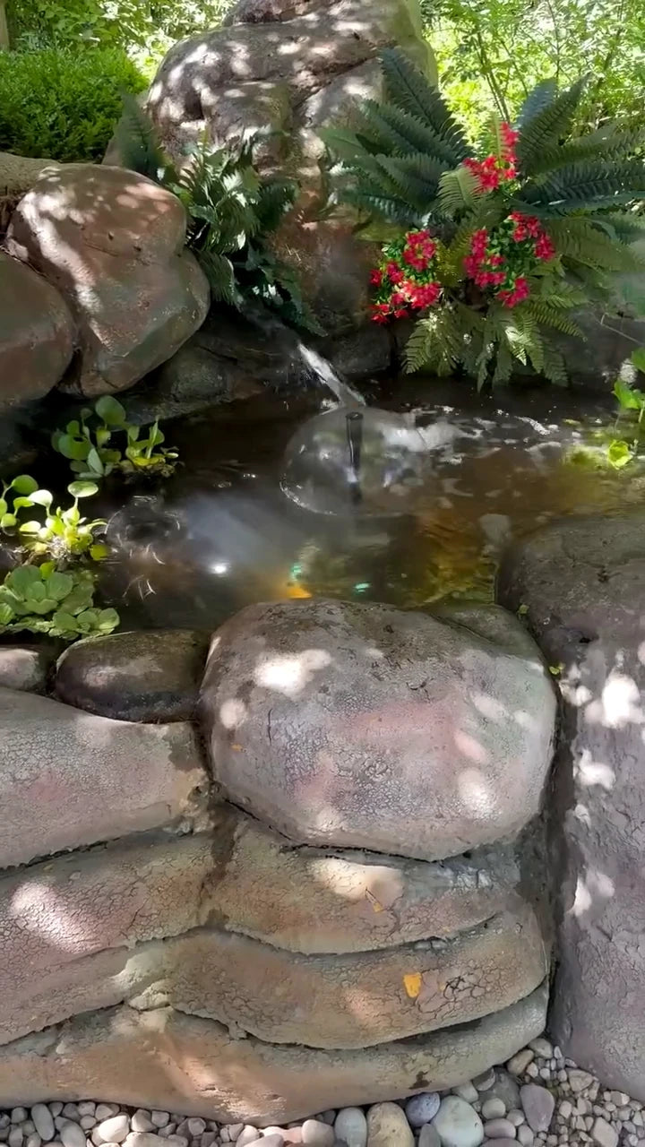 Flowing water in a naturalistic backyard rock pond framed by green foliage