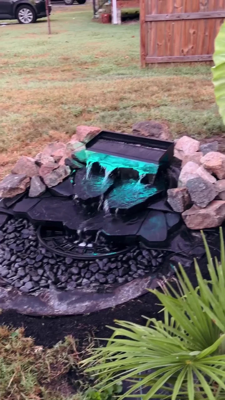 lilmilla’s completed black stone waterfall with turquoise-lit water and garden plants.